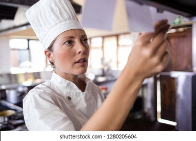 Female chef looking at order list in kitchen at hotel - Powered by Shutterstock