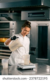 Female chef pouring water into a measuring glass standing on a kitchen scale in a professional kitchen