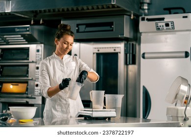 Female chef pouring water into a measuring glass standing on a kitchen scale in a professional kitchen