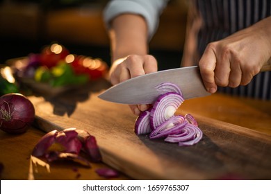Female chef is precisely slicing red onions on a wooden cutting board in a restaurant.  - Powered by Shutterstock