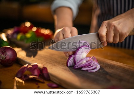 Female chef is precisely slicing red onions on a wooden cutting board in a restaurant. 