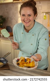 Female Chef Prepares Pancakes In A Bright Kitchen In A Rustic Style. Mint Coat Apron. Homemade Pancakes With Berries. Chef At Home