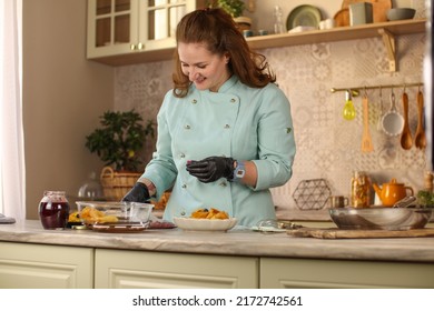 Female Chef Prepares Pancakes In A Bright Kitchen In A Rustic Style. Mint Coat Apron. Homemade Pancakes With Berries. Chef At Home