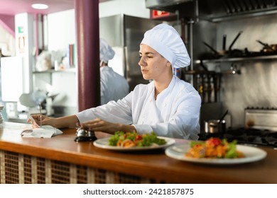 Female chef reads the paid check and presses the bell for visitors to the restaurant - Powered by Shutterstock