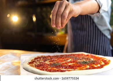 Female chef is sprinkling fresh oregano over a traditionally made home pizza.  - Powered by Shutterstock