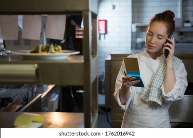 Female chef taking an order on the phone in the kitchen - Powered by Shutterstock