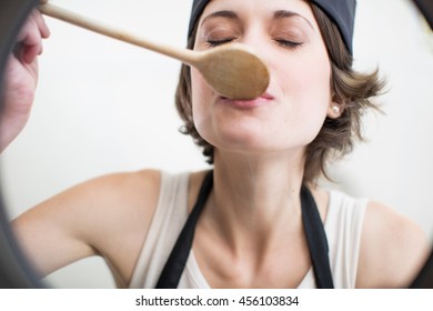 Female Chef Tasting Food From Saucepan In Commercial Kitchen