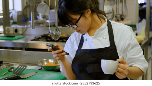 Female chef using mobile phone while having coffee in kitchen - Powered by Shutterstock