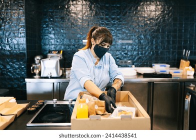 Female chef wearing face mask while keeping take out food in cardboard box at restaurant kitchen counter - Powered by Shutterstock