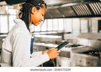 Female chef in world famous restaurant's modern kitchen cooks using tablet. Gourmet organic dishes prepared technology assists. Professional smiling reading communicating. - Powered by Shutterstock