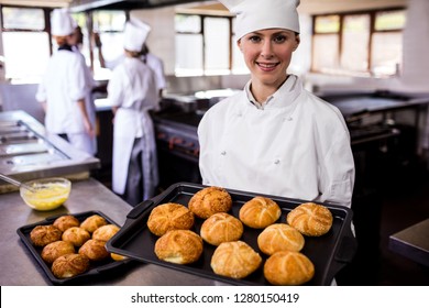 Female chefs holding baking tray of kaiser rolls in kitchen at hotel - Powered by Shutterstock