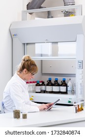 Female Chemical Scientist Holds Finger Over Blank Tablet Screen In Laboratory. Marijuana Bud, CBD And CBDa Oils Are On Table. Healthcare Pharmacy From Cannabis Seeds.