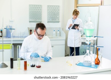 Female Chemical Scientist Holds Finger Over Blank Tablet Screen In Laboratory. Marijuana Bud, CBD And CBDa Oils Are On Table. Healthcare Pharmacy From Cannabis Seeds.