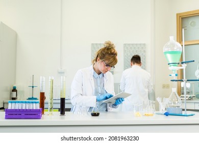 Female Chemical Scientist Holds Finger Over Blank Tablet Screen In Laboratory. Marijuana Bud, CBD And CBDa Oils Are On Table. Healthcare Pharmacy From Cannabis Seeds.