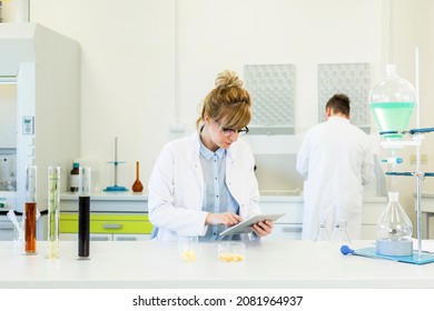 Female Chemical Scientist Holds Finger Over Blank Tablet Screen In Laboratory. Marijuana Bud, CBD And CBDa Oils Are On Table. Healthcare Pharmacy From Cannabis Seeds.