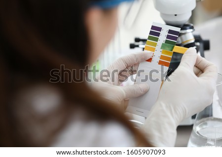 Female chemist holding litmus paper in hands. Analyzes ph test in a chemical laboratory. Chemistry industry education concept