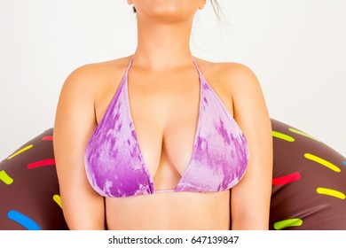 Female Chest Closeup. Young Attractive Unrecognizable Woman In Purple Ice Velvet Bikini Top With Donut Float. Mild Retouch, Closeup, Studio Lighting.