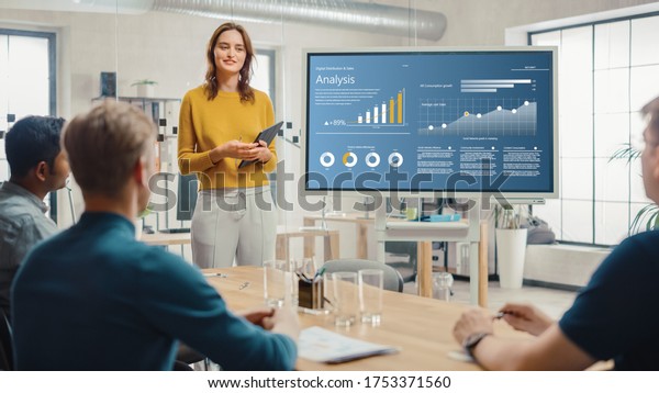 Female Chief Analyst Holds Meeting Presentation\
for a Team of Economists. She Shows Digital Interactive Whiteboard\
with Growth Analysis, Charts, Statistics and Data. People Work in\
Creative Office.