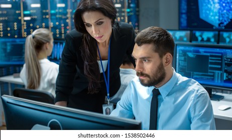 Female Chief Computer Engineer Consults Male Neural Network Architect. They Work In A Crowded Office On A Neural Network/ Artificial Intelligence Project. Office Space Has Data Server