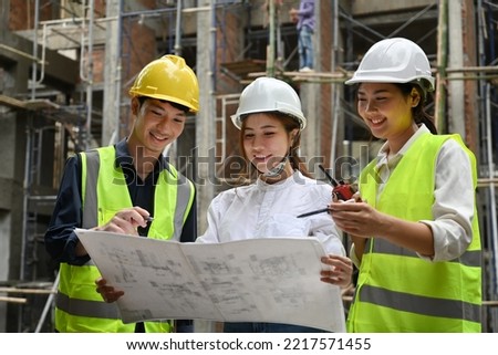 The female chief engineer and her assistant discuss building plans with the foreman.