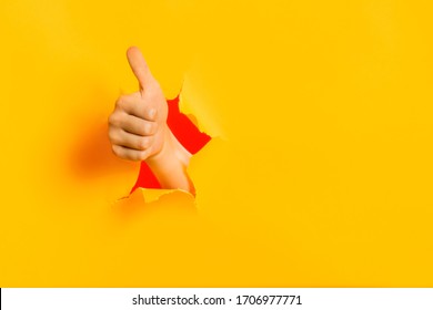 Female child hand gesturing the ok sign, like gesture through torn yellow paper wall, keeps thumb up. Approval sign, recommends something. Copy space fo text information. Best choice concept