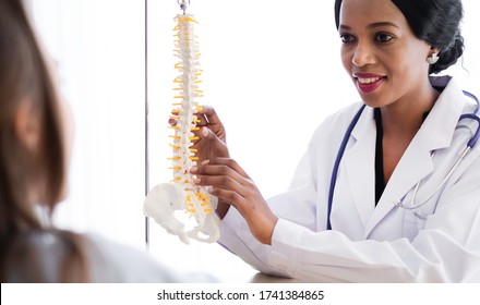 Female Chiropractor With Spine Bone Model Explaining Orthopedic Disorder To Patient In Hospital. Chiropractor Is Physiotherapist Who Can Give Bone Treatment. Chiropractor & Scoliosis Surgery Concept. 