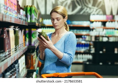 Female chooses and examines product on the supermarket shelves. household chemicals or body care goods detergents in store. Woman customer background reads and inspects a label shampoo make a purchase - Powered by Shutterstock