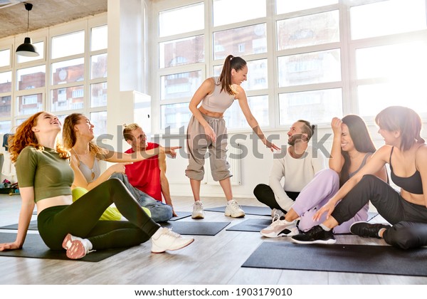 female choreographer explain the need\
for training and physical exercise before dancing, have talk, group\
of people sit on the floor listening to\
him