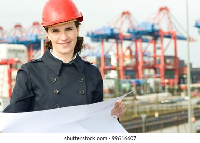 Female Civil Engineer Wearing Helm And Checking The Drawings In Front Of Industry Harbor Background