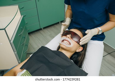 Female Client Of A Clinic Sits With His Mouth Open In A Dental Chair, Wearing Orange Safety Glasses. Dental Office. Dentistry. Stomatology.