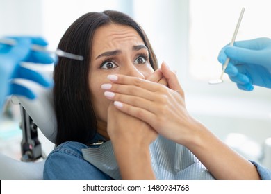 Female Client Covering Mouth With Hands Sitting In Dental Chair