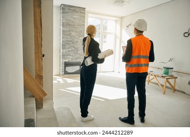 Female client and male engineer standing in room under construction - Powered by Shutterstock