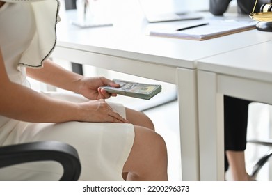 A female client tries to give money or bribe under a table to her lawyer. Bribe, Tribute, Graft, Corruption. - Shutterstock ID 2200296373