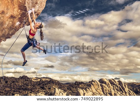 Female climber struggling up a sheer cliff.