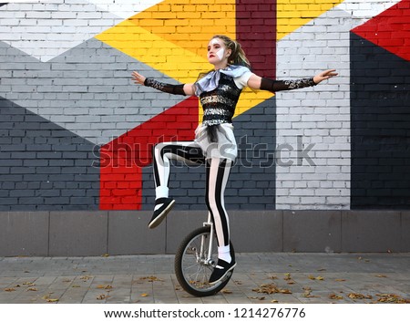 Female clown in circus clothes rides a unicycle outdoors
