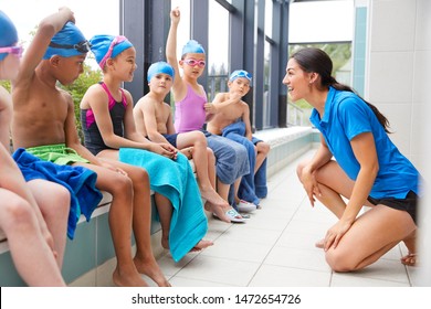 Female Coach Giving Children In Swimming Class Briefing As They Sit On Edge Of Indoor Pool - Powered by Shutterstock