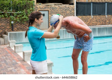 Female coach giving gold medal to senior man at poolside - Powered by Shutterstock