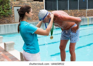 Female coach giving gold medal to senior man at poolside - Powered by Shutterstock