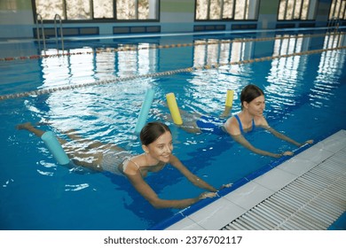 Female coach instructing young woman exercising with pool noodle aerobics class - Powered by Shutterstock