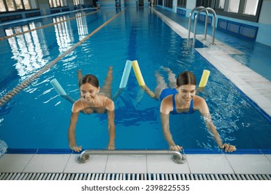 Female coach instructing young woman exercising with pool noodle aerobics class - Powered by Shutterstock