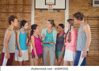 Female coach mentoring high school kids in basketball court - Powered by Shutterstock