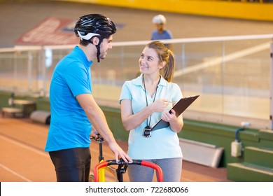 Female Coach Talking To Male Cyclist In Indoor Velodrome