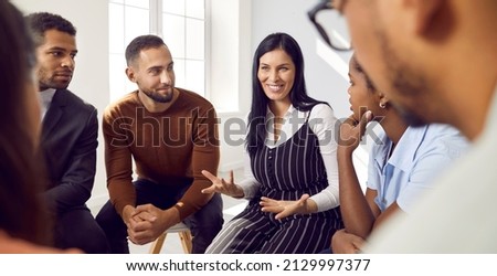 Female coach or team leader tells funny story or joke to diverse team during work meeting. Multiracial employees sitting in circle on chairs during informal brainstorming exchange ideas.