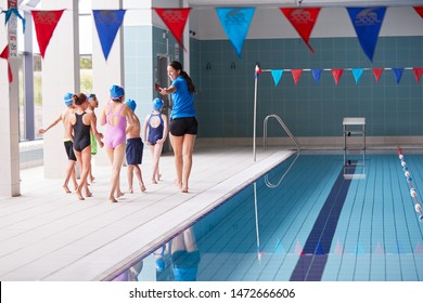 Female Coach Walks Children In Swimming Class Along Edge Of Indoor Pool - Powered by Shutterstock