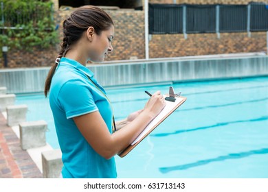 Female coach writing on clipboard near poolside - Powered by Shutterstock