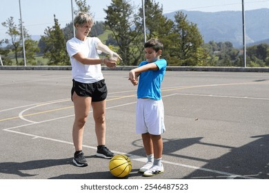 Female coach and young boy stretching arms before basketball practice on outdoor court - Powered by Shutterstock