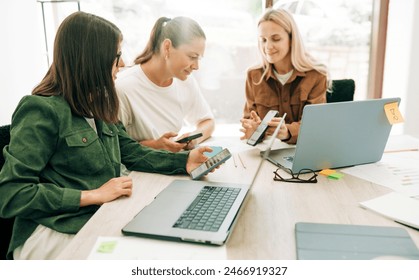 Female colleagues analyze social media marketing at a business meeting using mobile phone and laptops. - Powered by Shutterstock