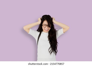 Female College Student Looks Depressed While Touching Her Head And Standing In The Studio With Purple Background