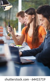 Female College Student Sitting In Library, Typing On Mobile Phone. Vertical Shape, Side View, Waist Up