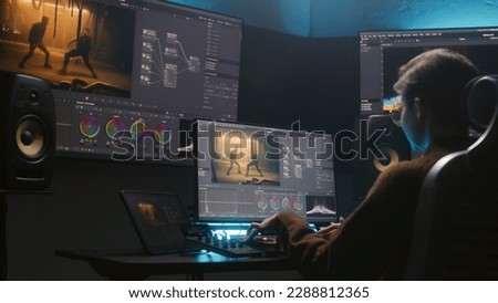 Female colorist uses color grading control panel, edits video, makes film color correction on computer in studio. Movie footage and RGB wheels on monitor. Big screens and tablet with program interface